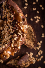 Close up of a stuffed chocolate easter egg with peanut and caramel on a wooden table with lots of peanuts around. Cracked. Top view. Selective focus.