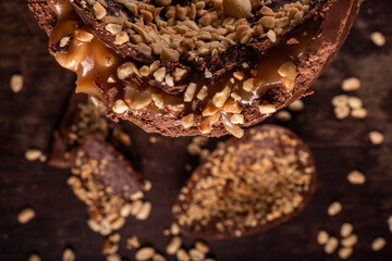 Close up of a stuffed chocolate easter egg with peanut and caramel on a wooden table with lots of peanuts around. Cracked. Top view. Selective focus.