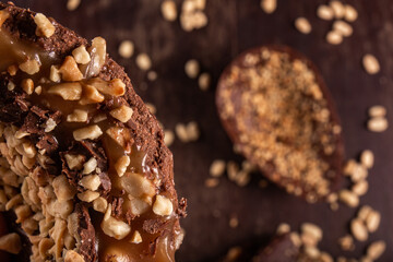 Close up of a stuffed chocolate easter egg with peanut and caramel on a wooden table with lots of peanuts around. Cracked. Top view. Selective focus.