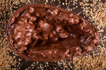 Stuffed chocolate easter egg with peanut and caramel on a wooden table with lots of peanuts around. Top view.