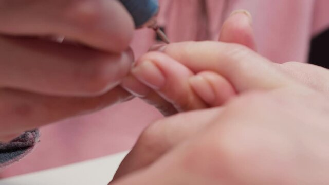 Manicurist uses metal nippers to remove dry skin of cuticle around nails. Process of manicure.