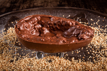 Stuffed chocolate easter egg with peanut and caramel on a wooden table with lots of peanuts around.