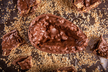 Stuffed chocolate easter egg with peanut and caramel on a wooden table with lots of peanuts around. Top view.
