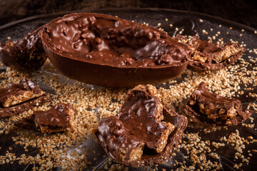 Stuffed chocolate easter egg with peanut and caramel on a wooden table with lots of peanuts around.