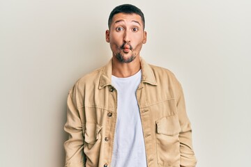 Handsome man with tattoos wearing casual brown denim jacket making fish face with lips, crazy and comical gesture. funny expression.