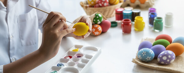 Happy Asian woman painting eggs for Eastertime at home. Family preparing for Easter.
