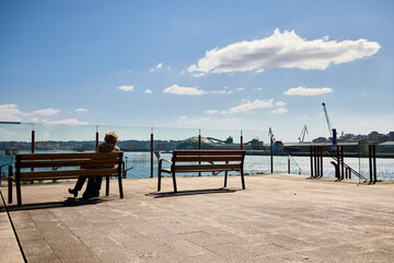 Fototapeta na wymiar Adult woman looking at the sea sitting on a wooden bench