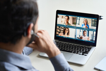 Indian business man wearing headset having virtual team meeting on video conference call using...