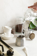 The process of making coffee in the home kitchen. Water is poured from a jug into a geyser coffee maker. Vertical orientation.