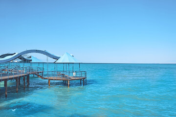 Azure sea water with pier under blue sky. Wooden bridge to ocean beach with metal carport. Nature summer landscape. Tourism background. Travel and vacation.