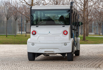Electric street vehicle with zero emission stands near the wall in the park. The road is paved with cobblestones. Compact electric utility vehicle to transport guests to and from an event.