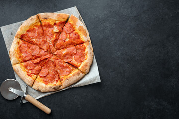 Tasty pepperoni pizza on black stone background. Pizza pepperoni cut into slices. Top view copy space for ad text or design