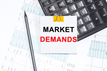 Text MARKET DEMANDS on NOTEBOOK ,NOTEBOOK, CALCULATOR PENCIL on white background.