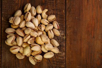 Pistachio nuts are sprinkled on a dark wooden table.