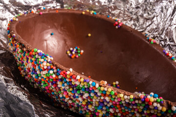 Close up of a colorful chocolate easter egg with sprinkles on an aluminium foil.