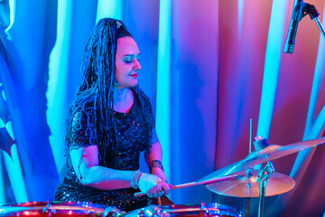 Woman with blue afro hairstyle musician drummer plays drums during a concert.