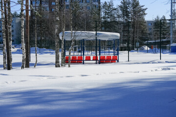 Naklejka premium Red chairs under a canopy in the snow on the football field.