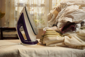  There is an iron and a large pile of non-ironed linen on the ironing board. An example of the need...