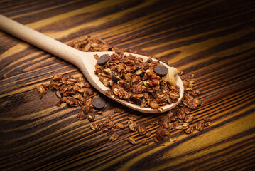 Chocolate granola cereal with nuts in a wooden spoon.