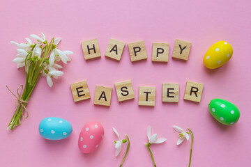 Delicate waterdrop flowers, colored eggs and the inscription Happy Easter on light pink background with copy space. Flat lay, top view