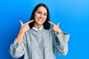 Young hispanic woman wearing casual clothes smiling cheerful showing and pointing with fingers teeth and mouth. dental health concept.