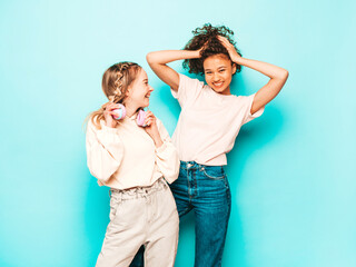 Two young beautiful smiling international hipster female in trendy summer clothes. Sexy carefree women posing near blue wall in studio. Positive models having fun. Concept of friendship