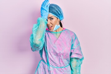 Young brunette woman wearing surgeon uniform and medical mask surprised with hand on head for...