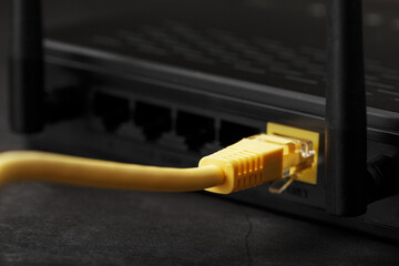 Wireless modem router with yellow cable and LAN port for connection on a black background.