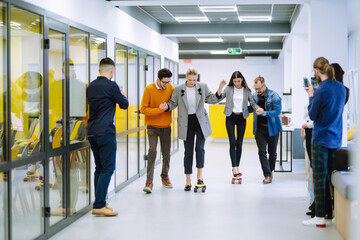 Group of coworkers having fun with skateboard in the office. Business people cheering when their colleagues skateboarding in the office. 