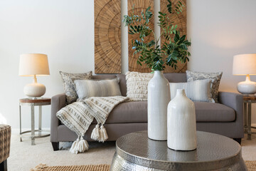 Detail of white vases with greenery on coffee table near gray couch with textured and pattern...