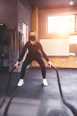 gyms at the time of the coronavirus. a woman with a mask on her face exercising with a rope in the gym.