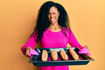 Middle age african american woman holding homemade bread winking looking at the camera with sexy...
