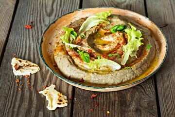 An oriental dish of baked eggplant babaganush (eggplant puree) with spices, herbs, lettuce and oriental flatbreads on wooden background.