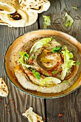 An oriental dish of baked eggplant babaganush (eggplant puree) with spices, herbs, lettuce and oriental flatbreads on wooden background.