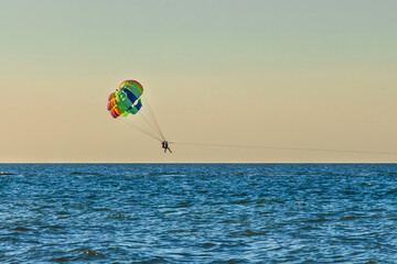 Man and woman tourists are flying on parasailing over the sea against the backdrop of the sunset sky and the horizon. Extreme vacation concept