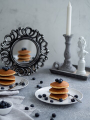 Pankety with blueberry on gray background with mirror and candle
