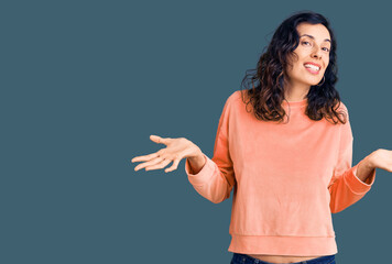 Young beautiful hispanic woman wearing casual clothes clueless and confused expression with arms...