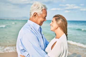 Middle age hispanic couple smiling happy and hugging walking at the beach