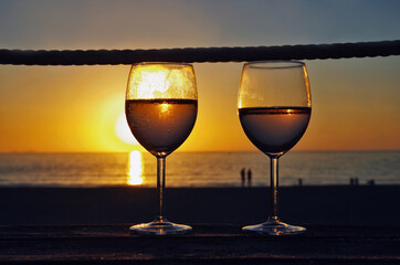 Close up two glasses of white wine, sunset on the beach in the background. Drink on the beach. Romantic evening.