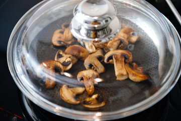 View from above of frying pan covered with glass lid of fresh mushrooms