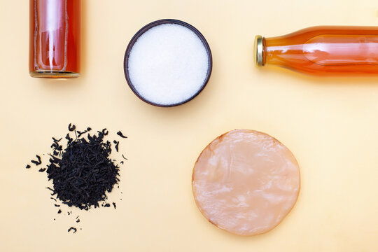 Two Bottles Of Kombucha Tea, Scoby, Brew And Bowl Of Sugar On Yellow Pastel Background. Ingredients For Preparing Healthy Fermented Drink. Flatlay Mockup