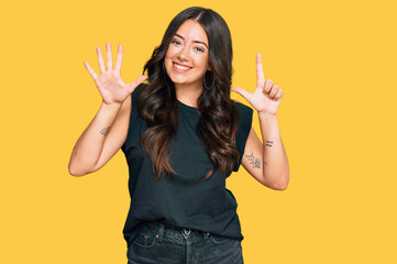 Beautiful brunette young woman wearing black shirt showing and pointing up with fingers number seven while smiling confident and happy.