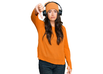 Fototapeta premium Beautiful brunette young woman listening to music using headphones looking unhappy and angry showing rejection and negative with thumbs down gesture. bad expression.