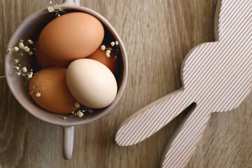 Ceramic bowl with eggs and gypsophila flowers and wooden bunny decoration. Easter decorations on wooden table. Flat lay. - Powered by Adobe