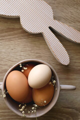 Ceramic bowl with eggs and gypsophila flowers and wooden bunny decoration. Easter decorations on wooden table. Flat lay.