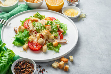Caesar salad close-up on a white plate surrounded by ingredients on a gray background.