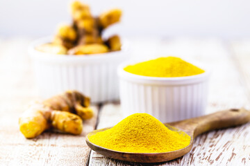 spoonful of powdered turmeric roots, turmeric in wooden bowl on white table