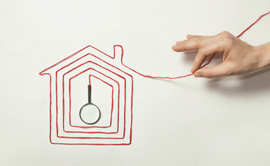 The human hand pulls on the thread laid out in the shape of a house with a magnifier at the end.