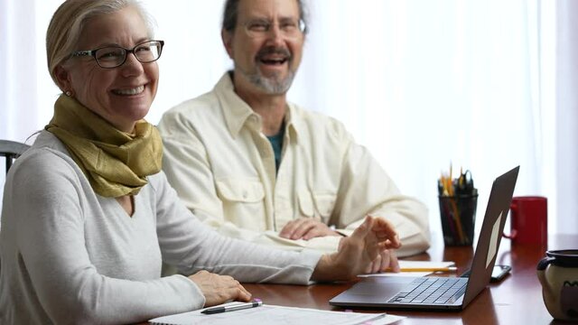 Portrait of mature man and woman at home working on laptop computer doing taxes and get good report. Concept of success couple working together.