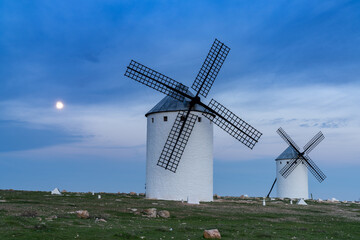 the historic white windmills of La Mancha above the town of Campo de Criptana at night under a full moon